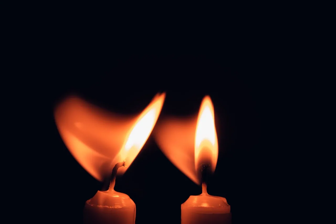 Two candle flames burning side by side in soft darkness