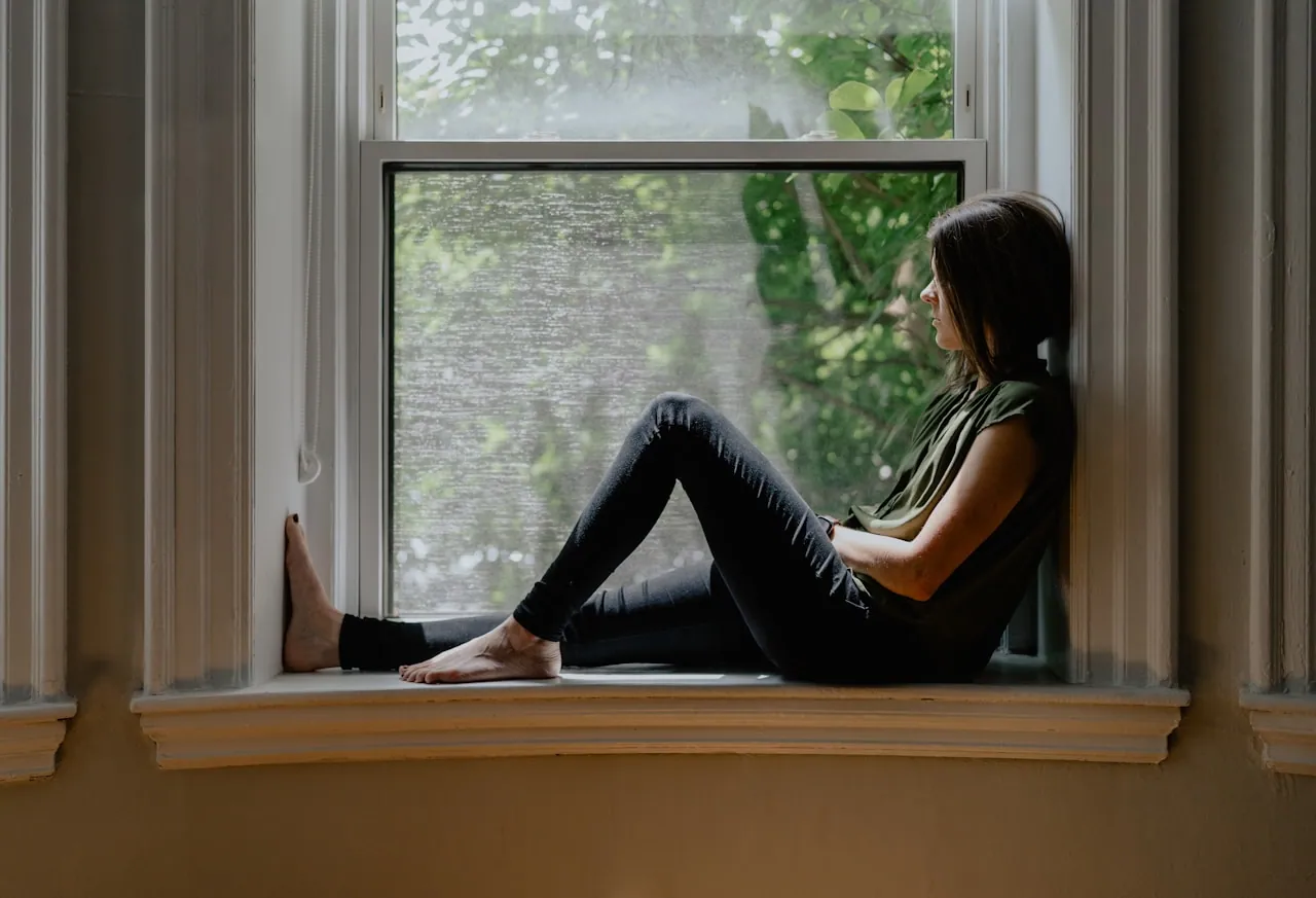 Woman sitting by a window in soft morning light, looking thoughtful